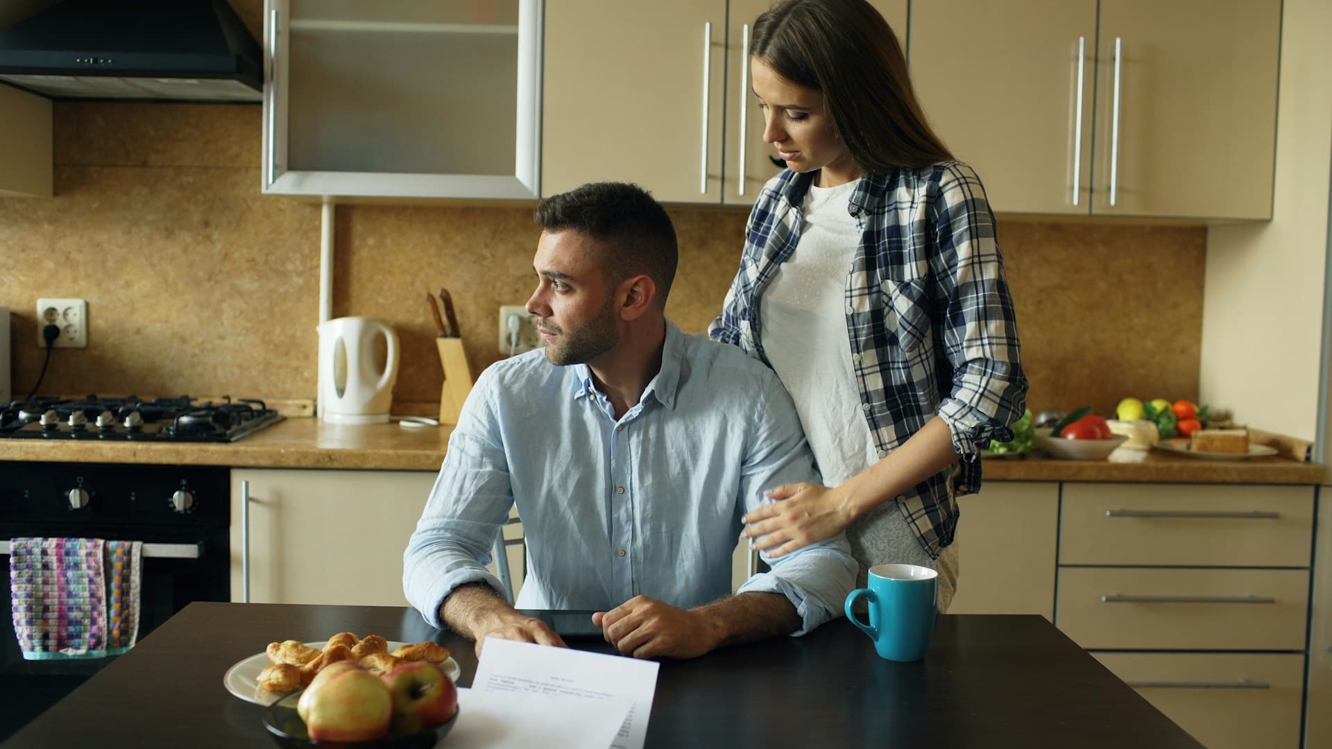 Couple at a kitchen table looking over paperwork together, with a mug and breakfast items nearby
